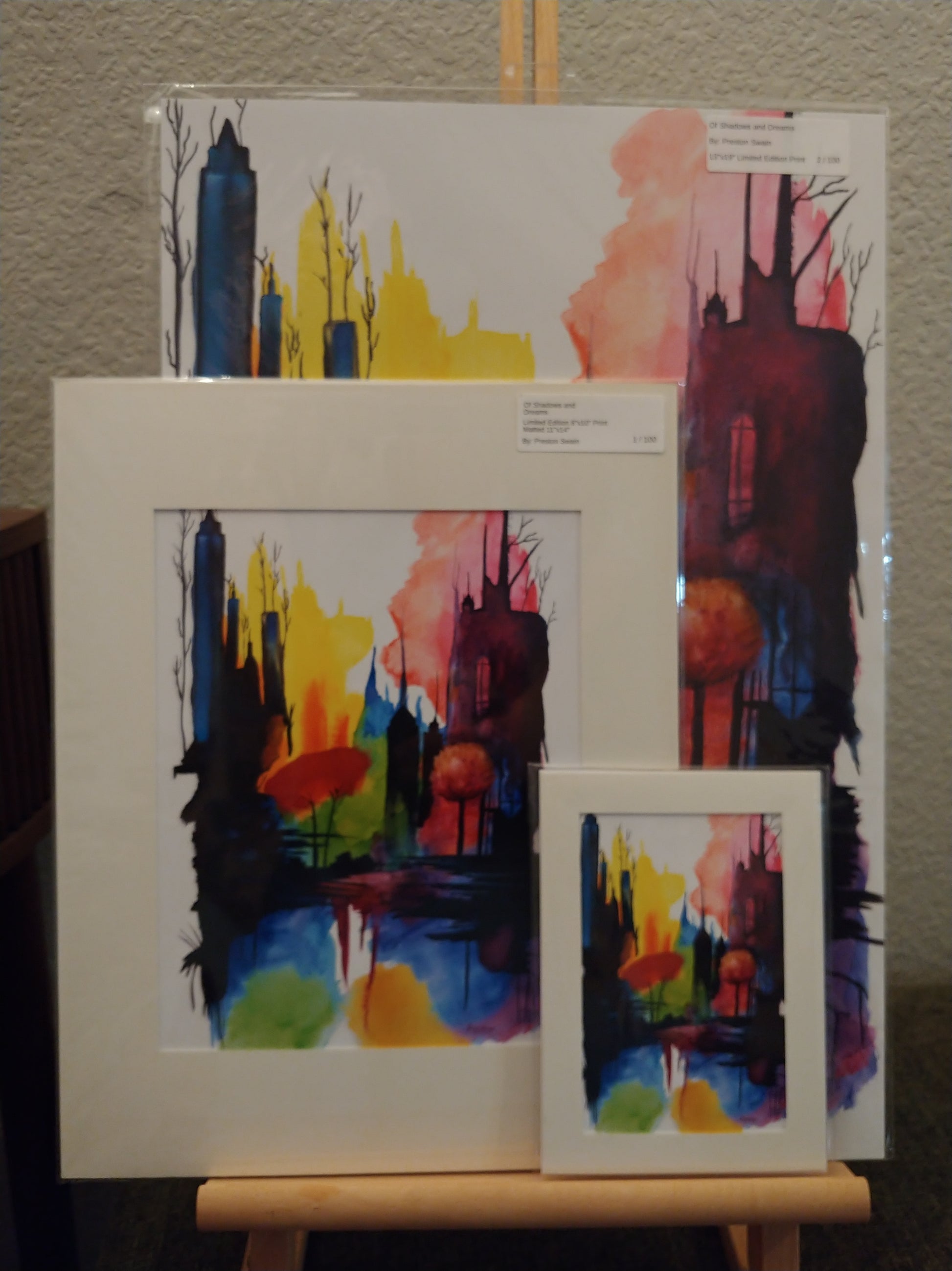 Set of abstract art prints on a wooden easel against a neutral background